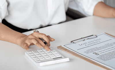 Person using calculator near loan agreement clipboard.